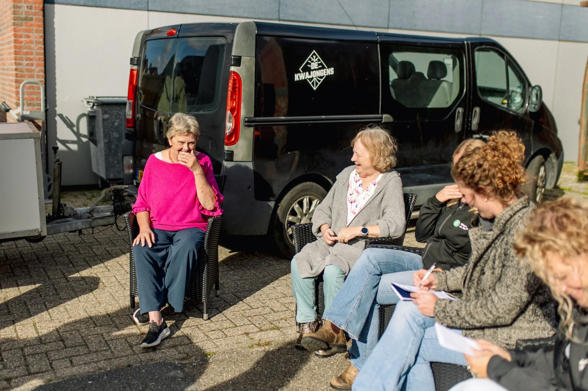 Groep mensen die buiten zitten en praten in de zon.