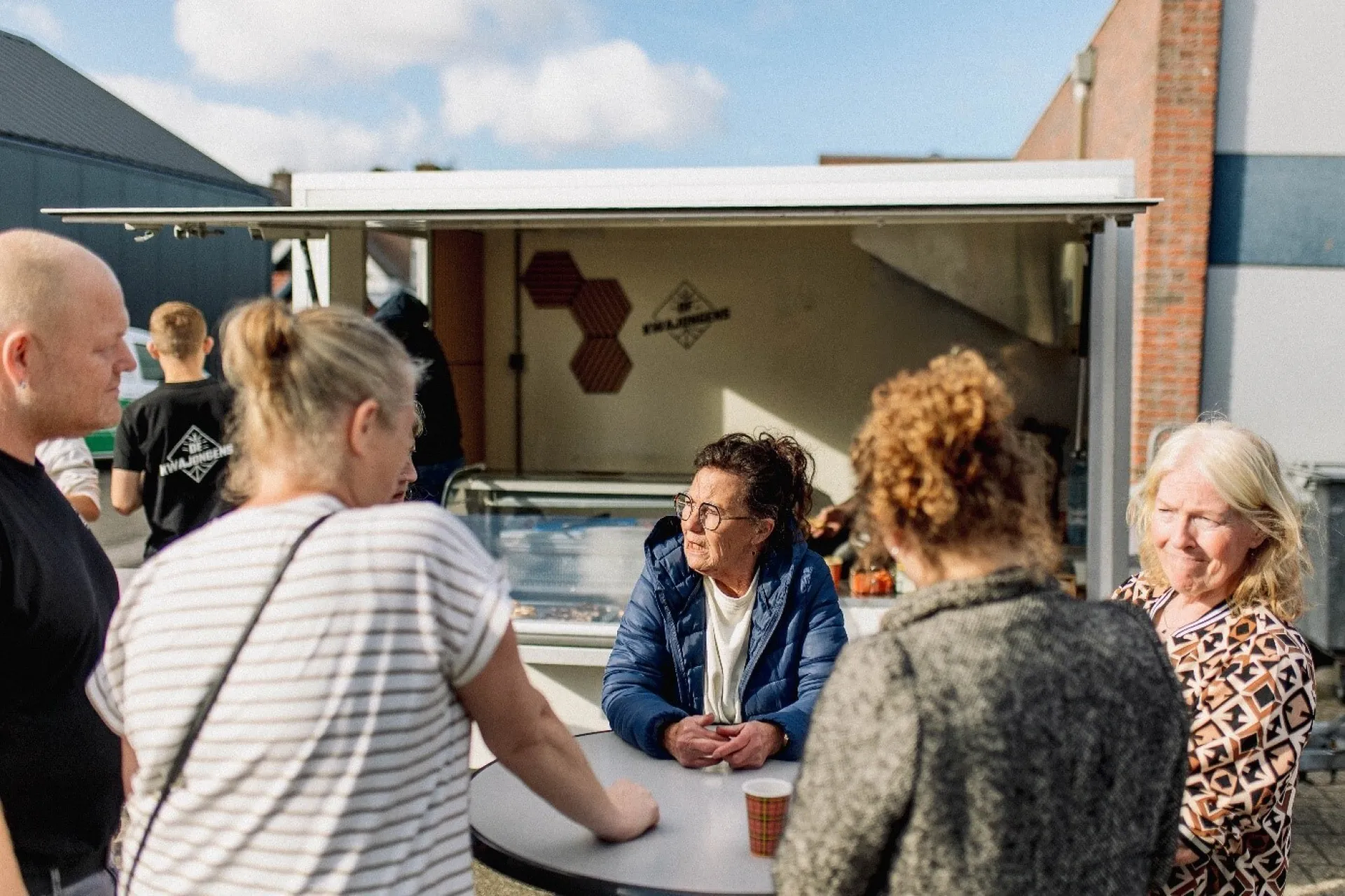 Groep mensen in gesprek bij een foodtruck.